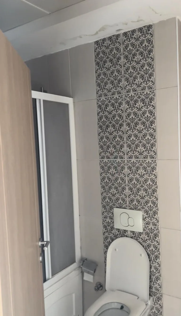 Dönüşüm öncesi banyo — desenli seramik şerit ve duşakabin